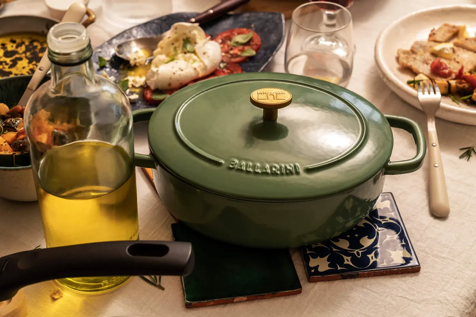 A green Ballarini cocotte on a lunch table with olive oil, tomatoes and bread